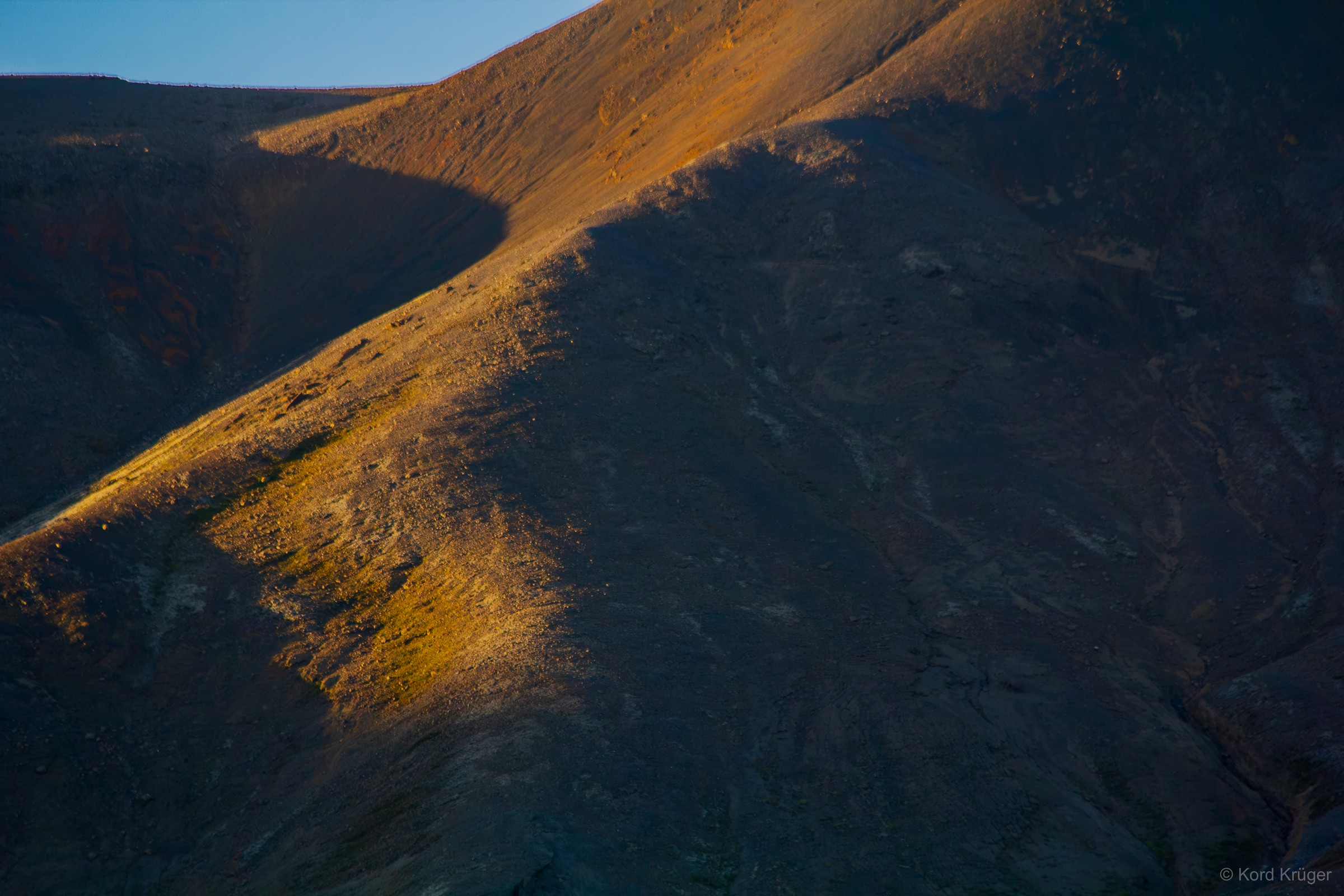 Warmes Licht streift einen steilen Berghang; ein tiefer Schatten teilt die braune Landschaft in klare Flächen.